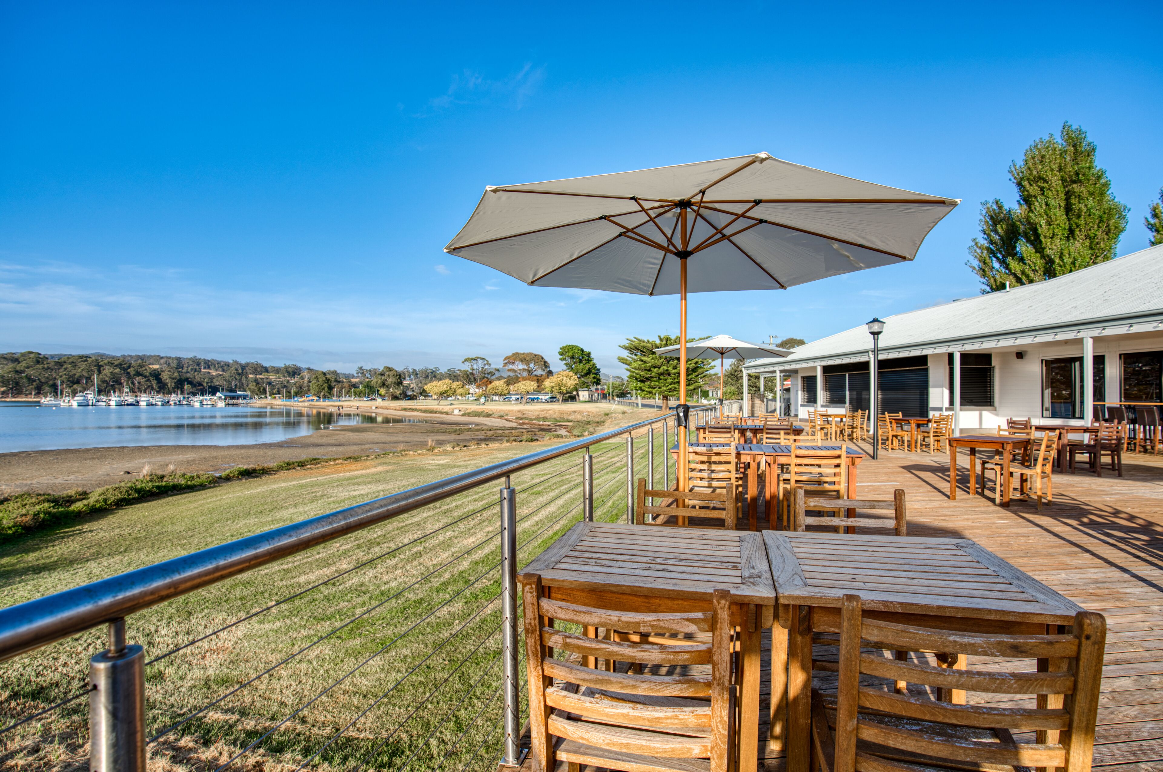 A wooden deck with tables and chairs, overlooking a body of water and a grassy area.