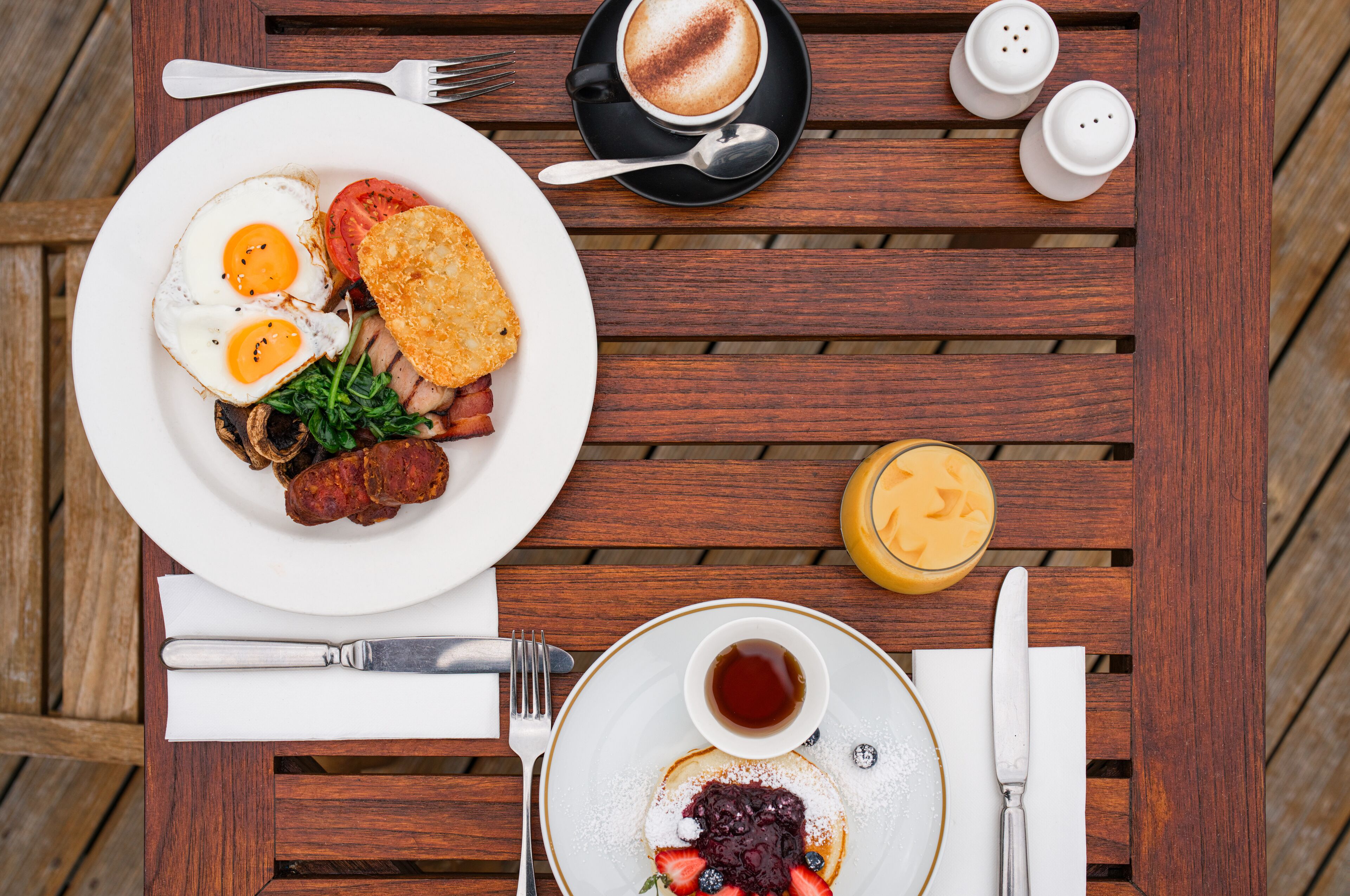 A wooden table with a breakfast plate containing eggs, bacon, and toast, a cup of coffee, and a glass of orange juice.