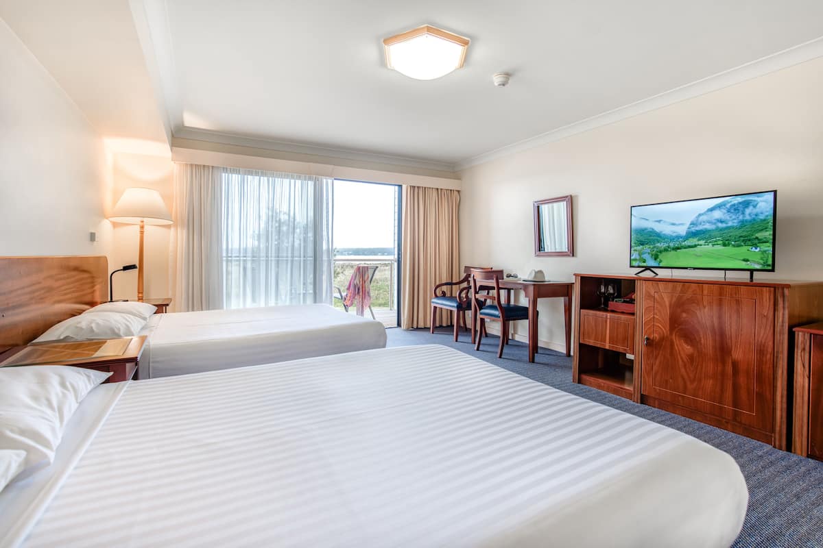 Quarto de hotel com duas camas, uma escrivaninha, televisão e vista para uma paisagem montanhosa.