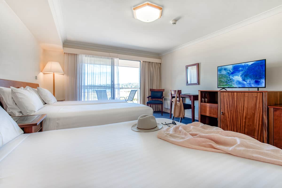 Quarto de hotel com duas camas, televisão, escrivaninha e uma cadeira.
