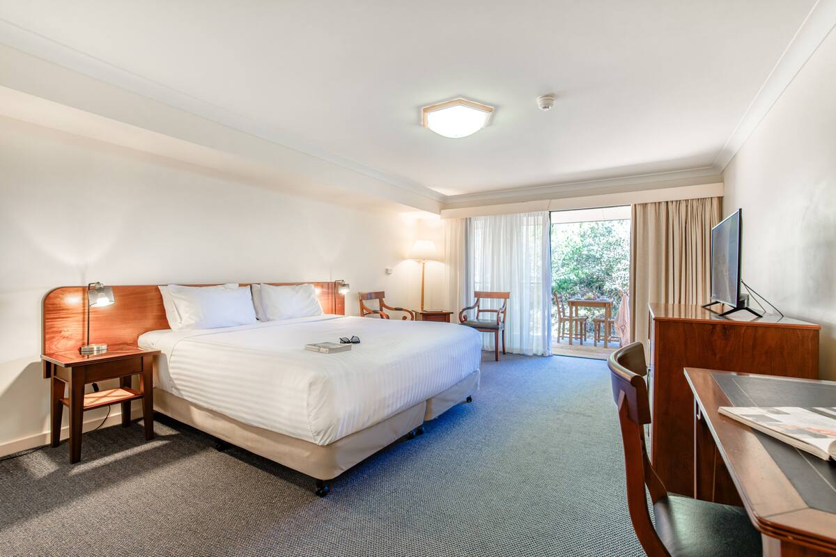 Quarto de hotel com uma cama grande, uma escrivaninha, uma cadeira, um abajur e uma televisão.