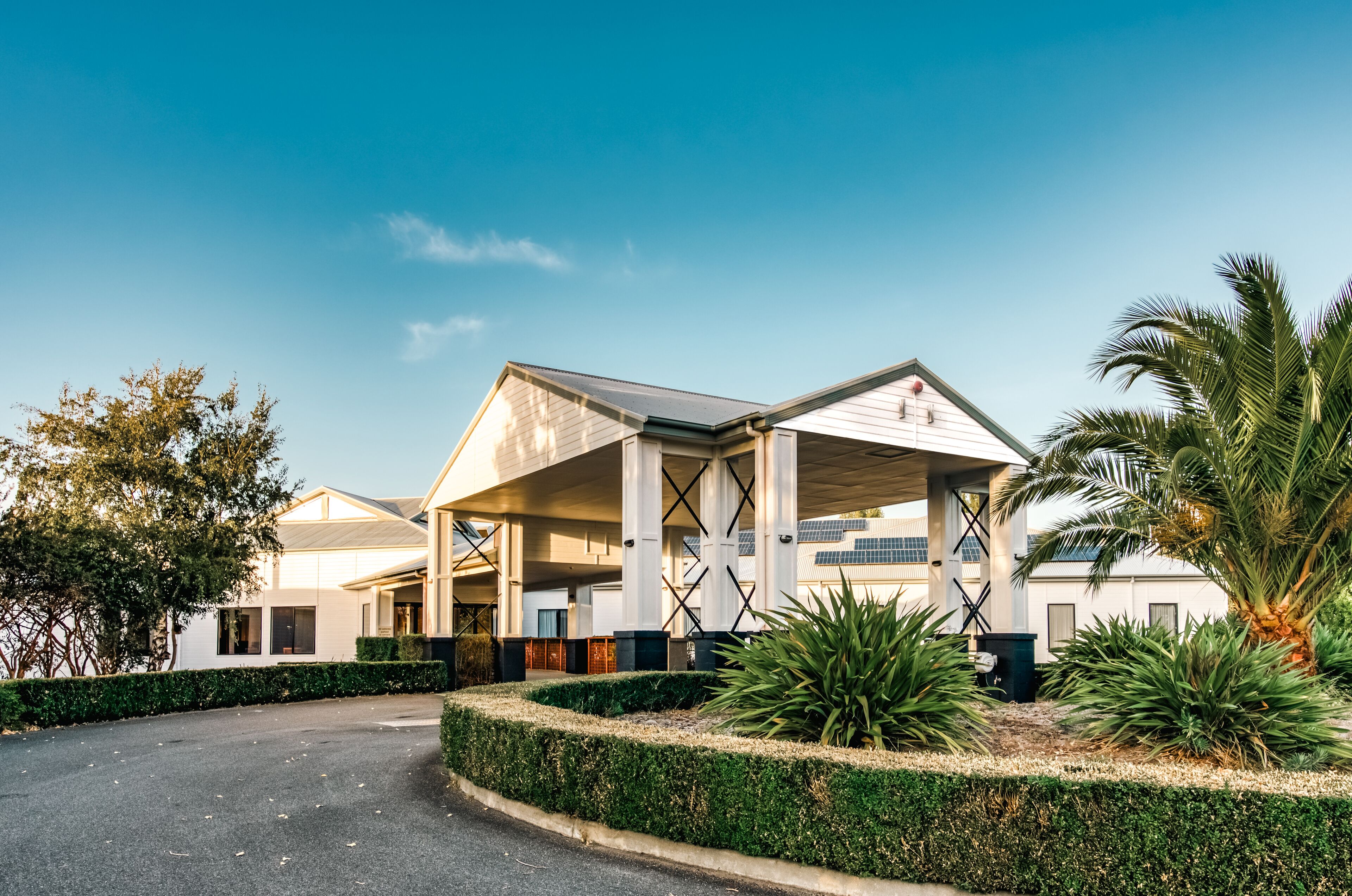A modern building with a covered outdoor area, surrounded by well-maintained landscaping and palm trees.