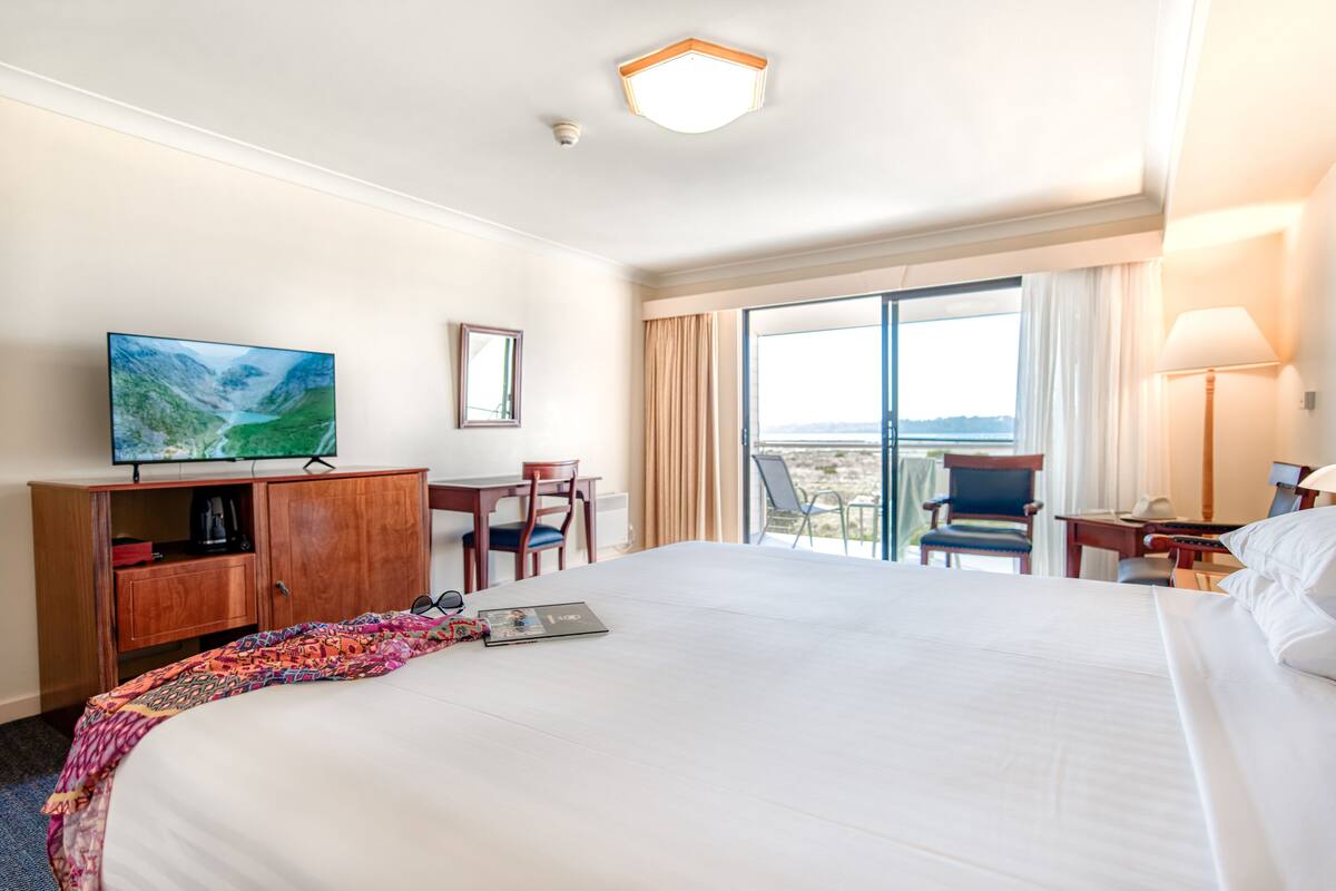 Quarto de hotel com uma cama grande, uma escrivaninha, uma televisão e vista para o exterior.