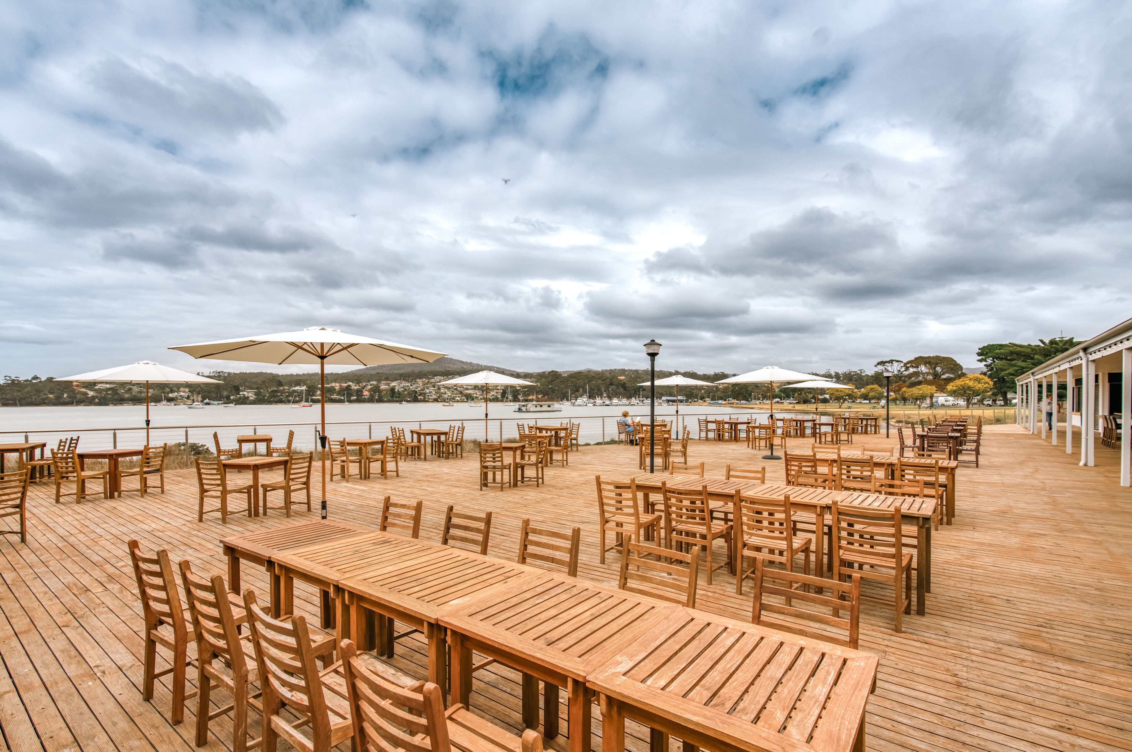 A wooden deck with tables and chairs, umbrellas, and a view of a body of water.