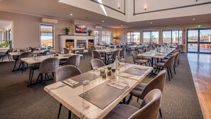 A spacious dining area with multiple tables and chairs, large windows, and a fireplace.