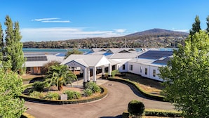 A modern hotel with solar panels on the roof, a landscaped garden, and a view of a lake and hills in the background.