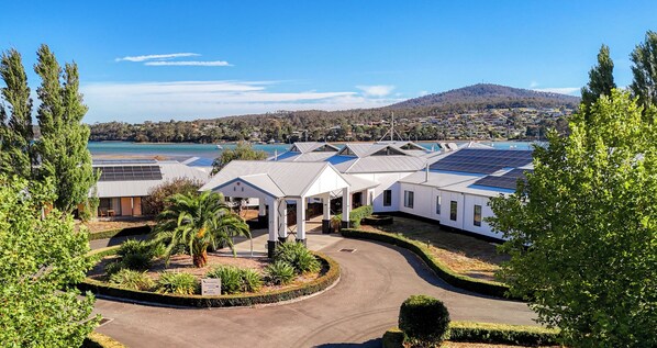 A modern hotel with solar panels on the roof, a landscaped garden, and a view of a lake and hills in the background. - Panorama Hotel St Helens (St Helens)