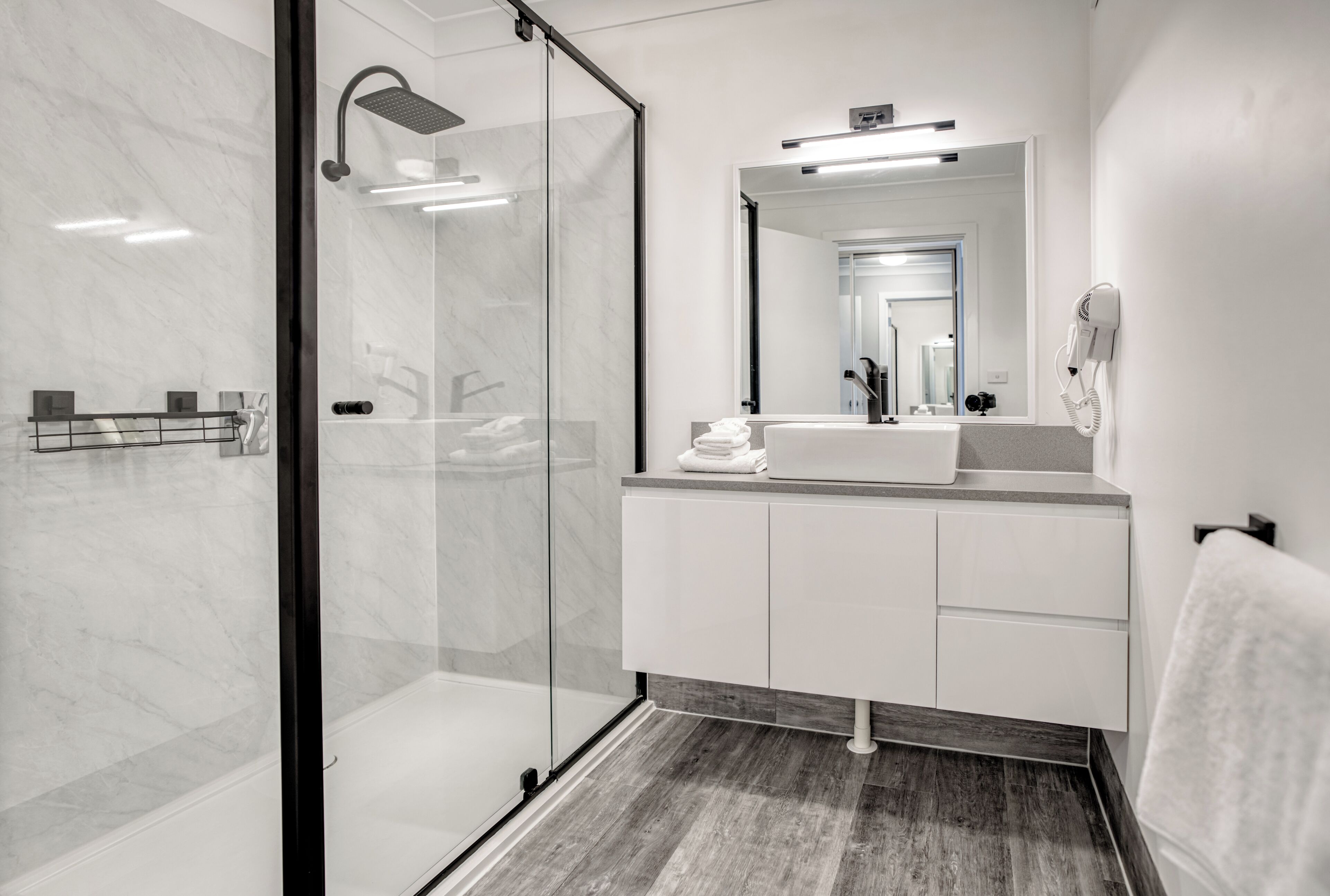 A modern bathroom with a glass shower enclosure, a white vanity with a mirror, and a towel rack.