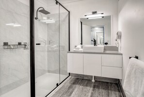 A modern bathroom with a glass shower enclosure, a white vanity with a mirror, and a towel rack. - Panorama Hotel St Helens (St Helens)