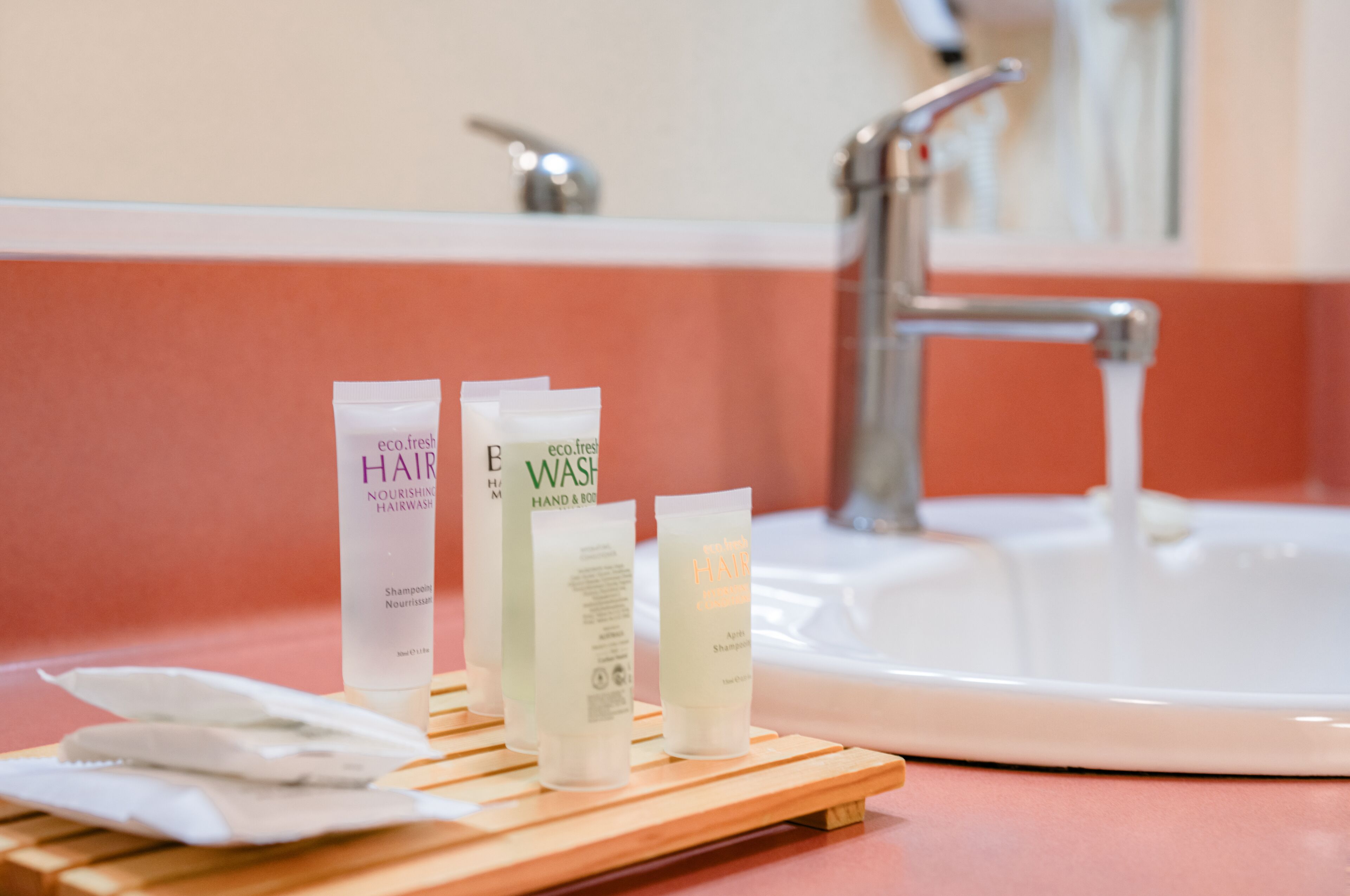 A bathroom with a sink, a mirror, and three hair care products on a wooden tray.