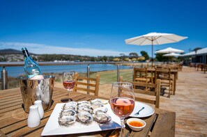 A table with a bottle of rosé wine, a glass of rosé wine, a plate of oysters, salt shakers, and a small bowl of sauce. - Panorama Hotel St Helens (St Helens)