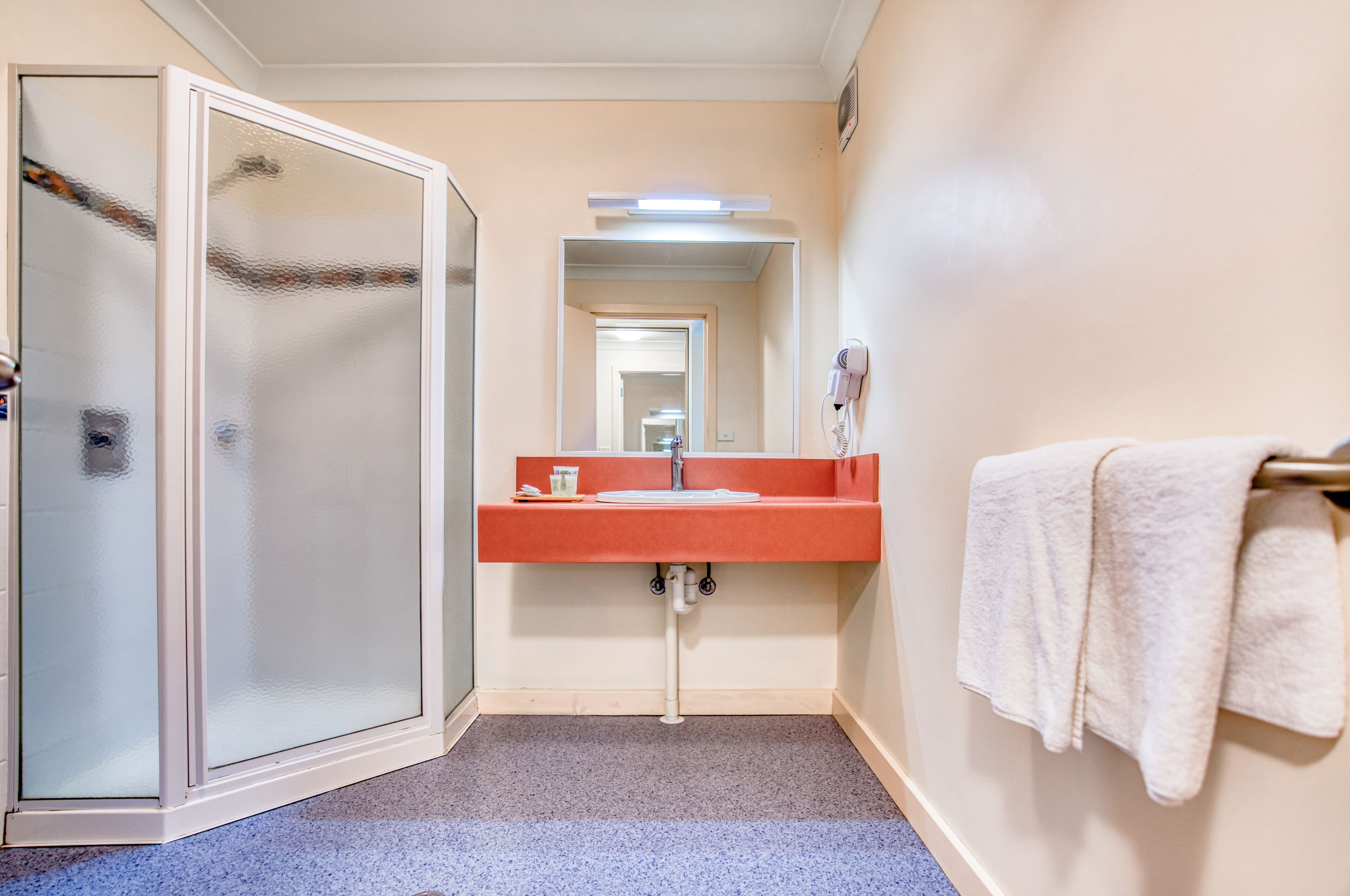 A bathroom with a glass shower enclosure, a sink with a red countertop, and a towel rack with towels.