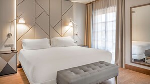 A hotel room with a large bed, two bedside lamps, a bench, and a mirror. - NH Collection León Plaza Mayor (León)
