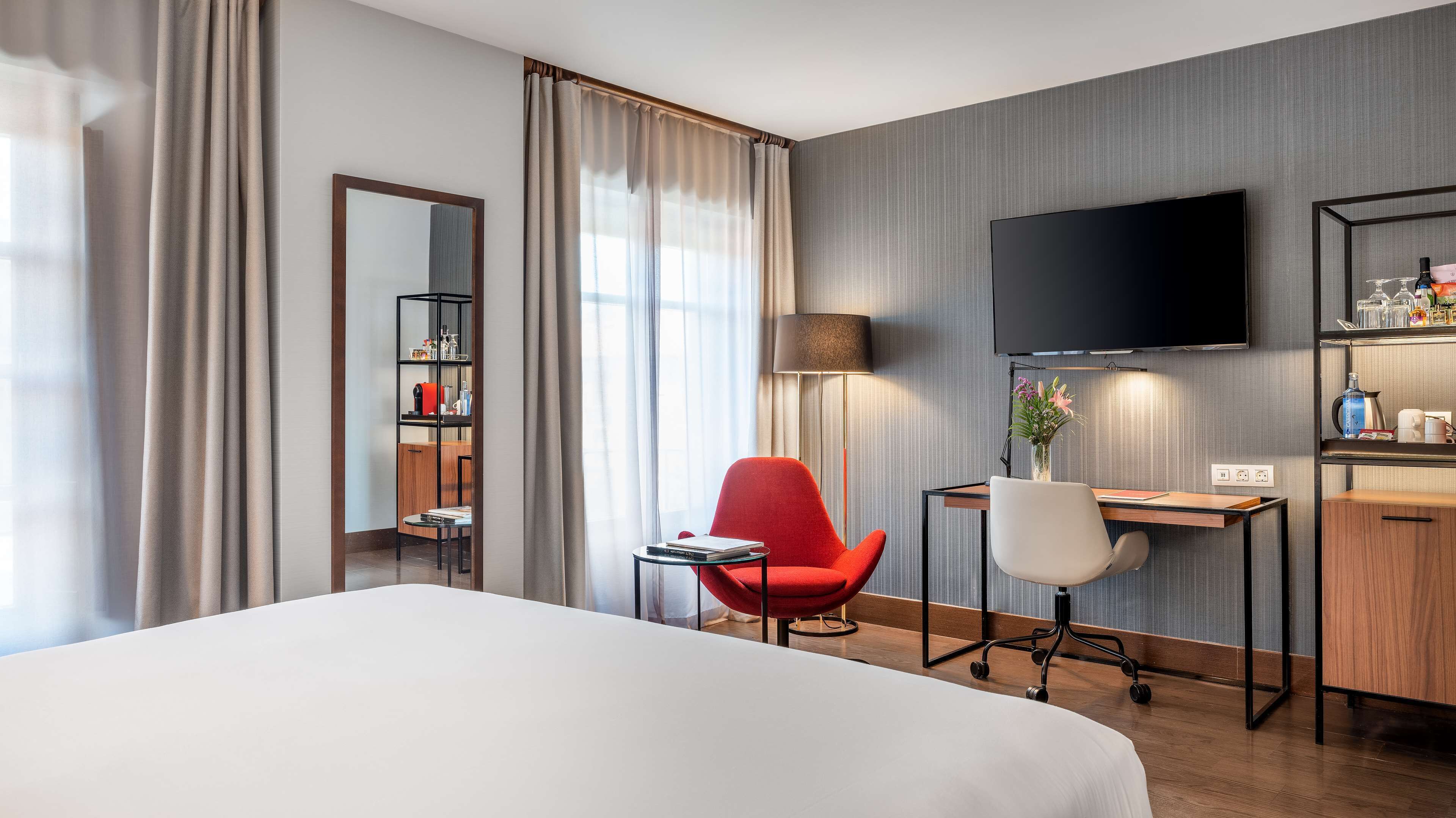 Habitación de hotel con cama, escritorio con silla, televisión, estantería y lámpara.