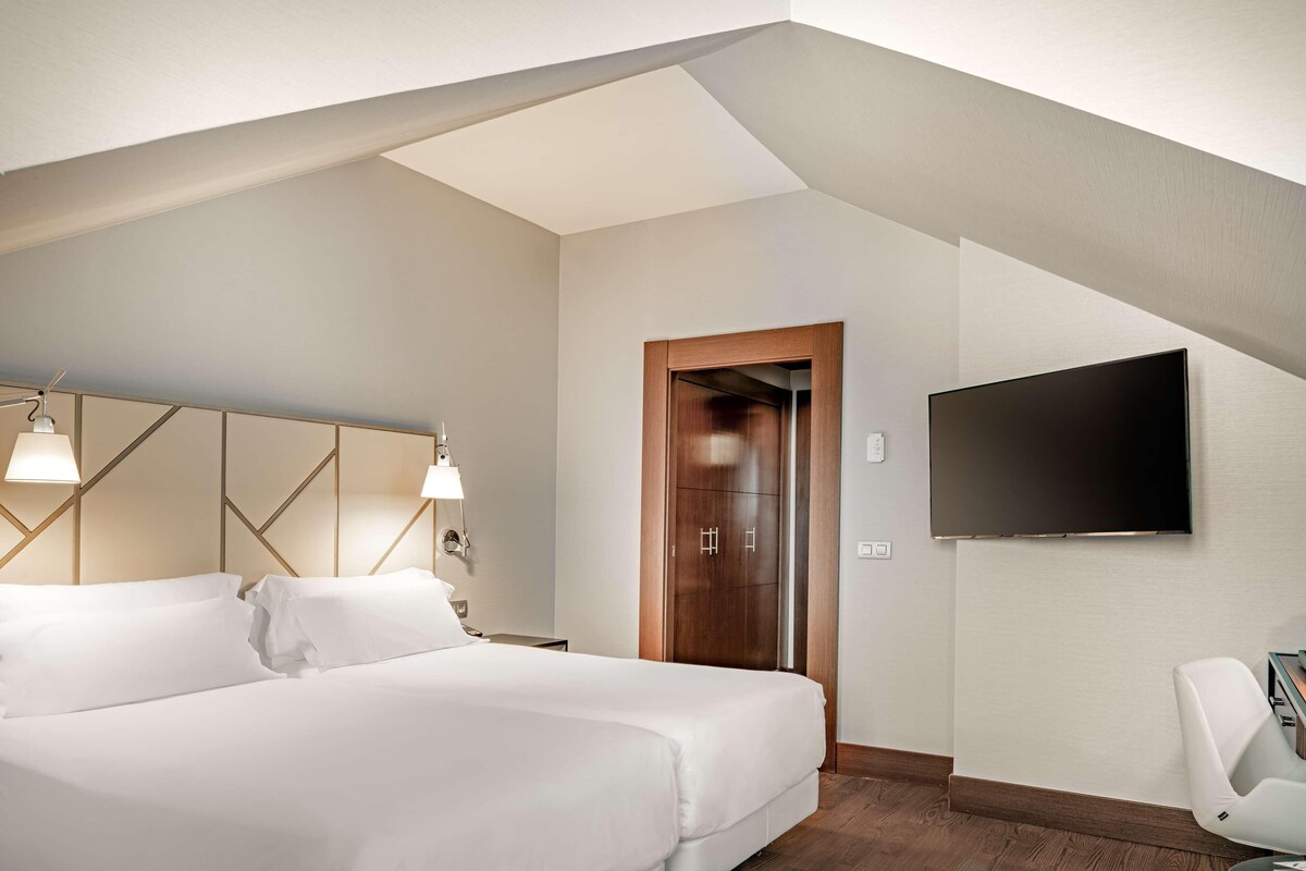 A modern hotel room with a large bed, a flat-screen TV mounted on the wall, and a wooden wardrobe.