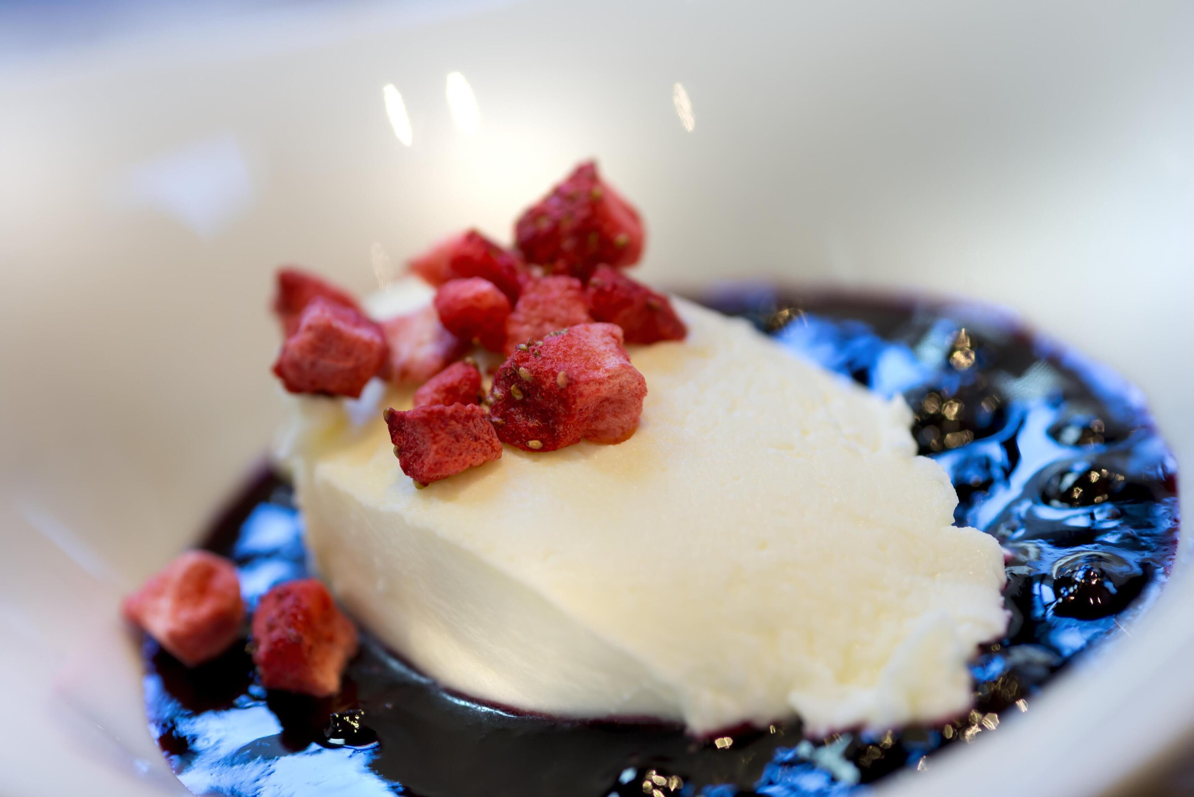 Un dessert composé d’une boule de glace servie dans une assiette, accompagnée de fruits rouges et d’une sauce au chocolat.