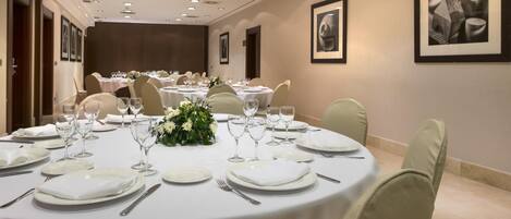 A conference room with round tables set for dining, equipped with white tablecloths, plates, cutlery, and wine glasses.