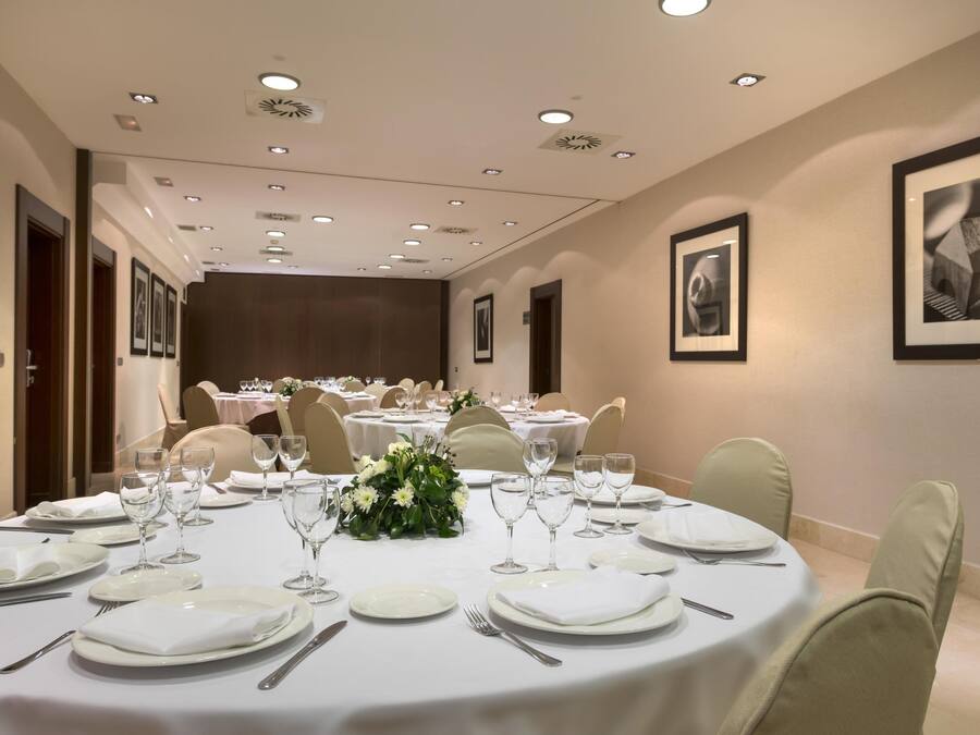 A conference room with round tables set for dining, equipped with white tablecloths, plates, cutlery, and wine glasses.