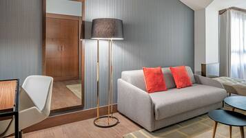 Een moderne hotelkamer met een bank, een staande vloerlamp, een bureau en een spiegel.