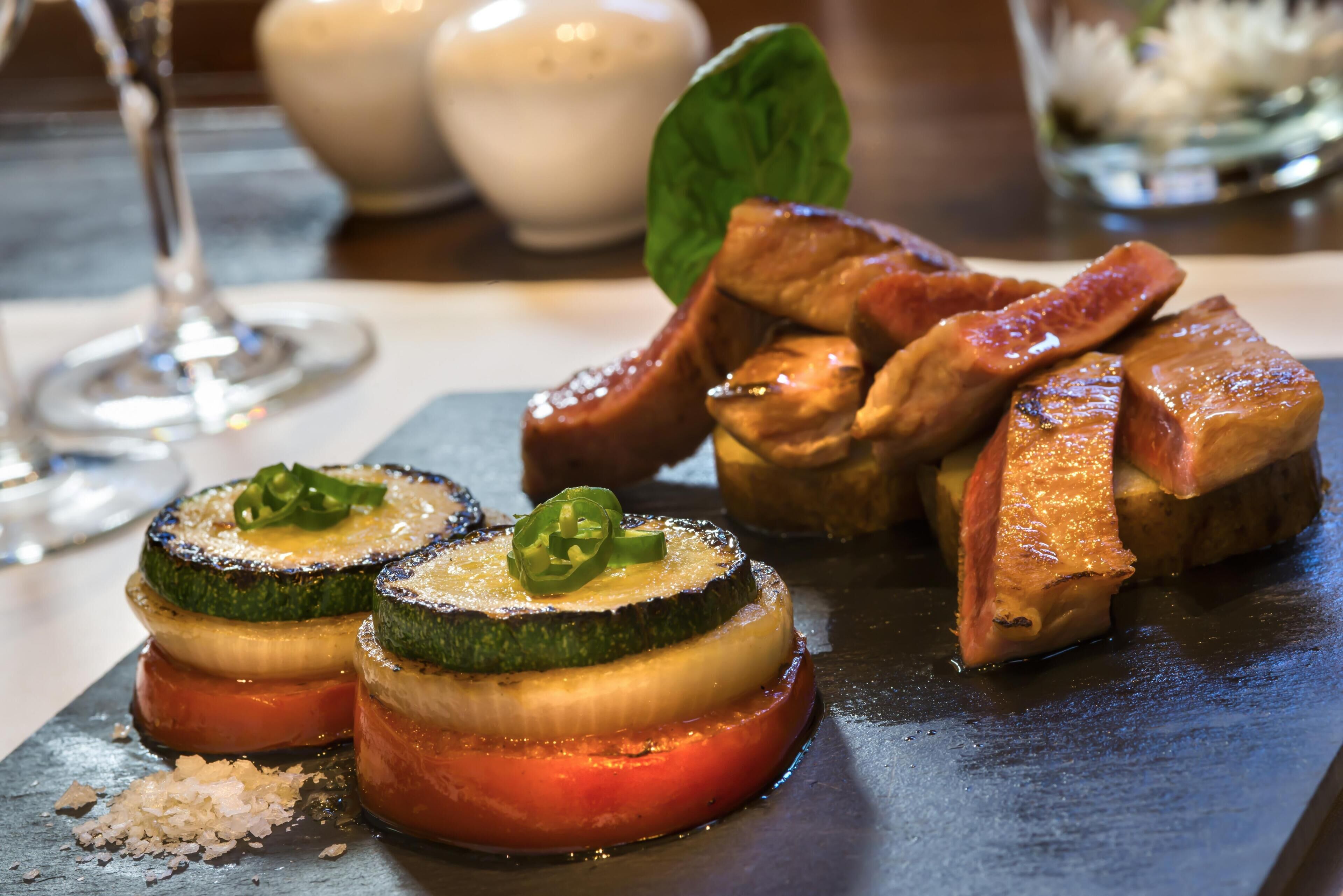 Un plato de rodajas de calabacín rellenas, con guarnición, servido sobre una tabla de pizarra.