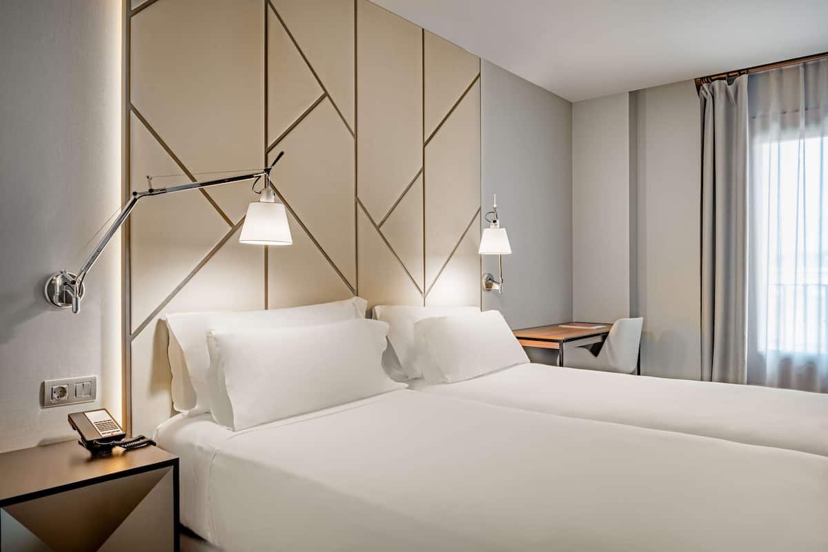 A hotel room with a large bed, two bedside lamps, a desk, and a chair.