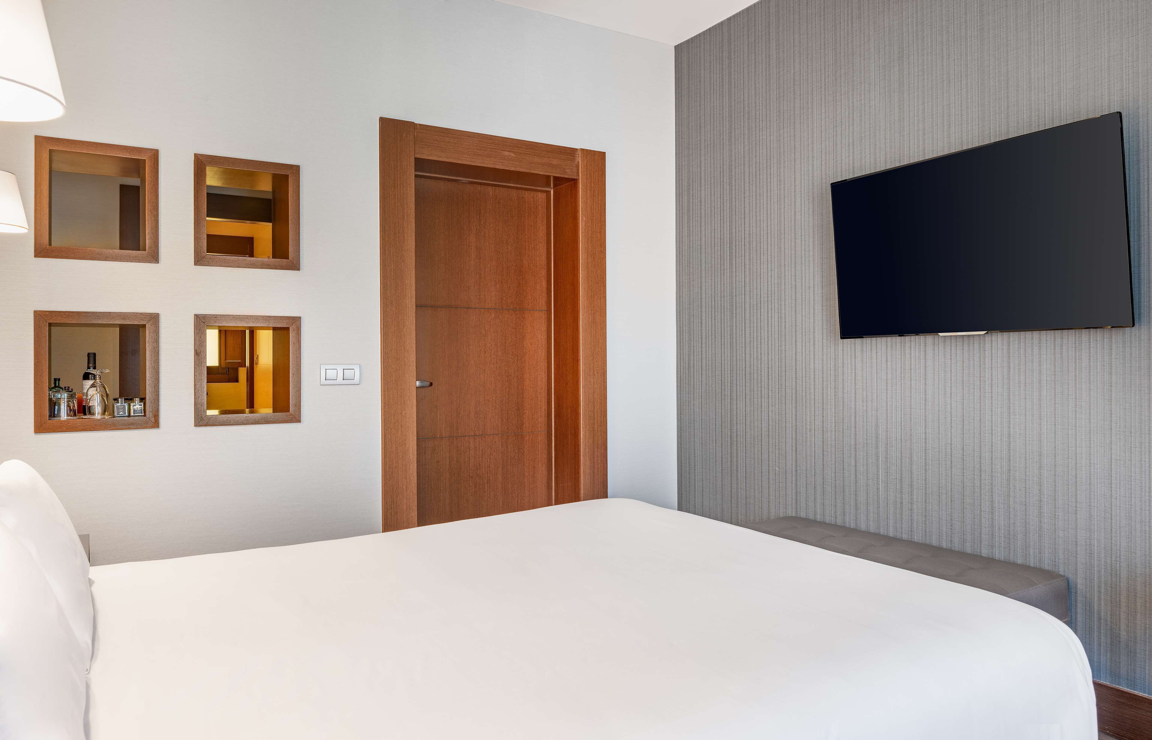 Una habitación de hotel con una cama grande, un televisor montado en la pared y una puerta de madera.