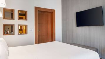 Una habitación de hotel con una cama grande, un televisor montado en la pared y una puerta de madera.