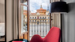 A room with a red chair, a black table, and a view of a historic building with a clock tower. - NH Collection León Plaza Mayor (León)