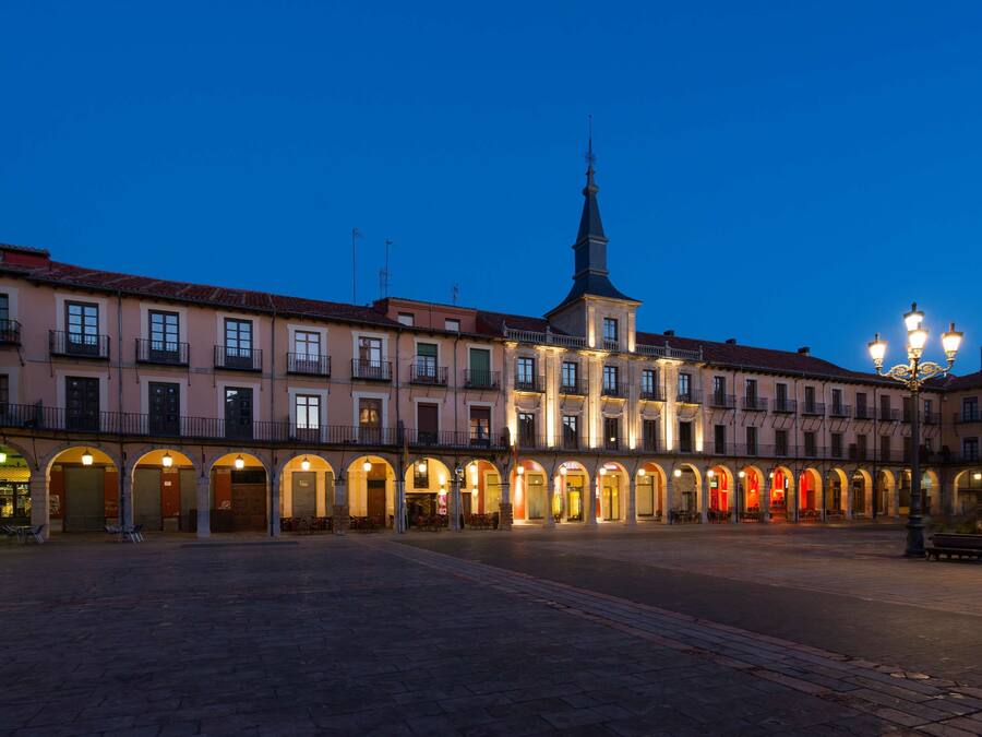 Una plaza histórica con una imponente torre de iglesia, arcadas y edificios tradicionales.