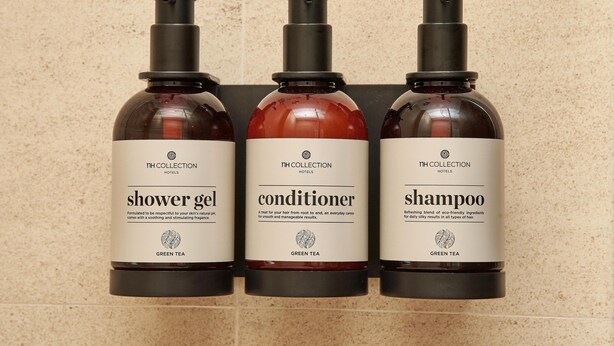 Tres botellas de artículos de aseo de hotel etiquetadas como 'gel de ducha', 'acondicionador' y 'champú', con la marca 'green tea'.