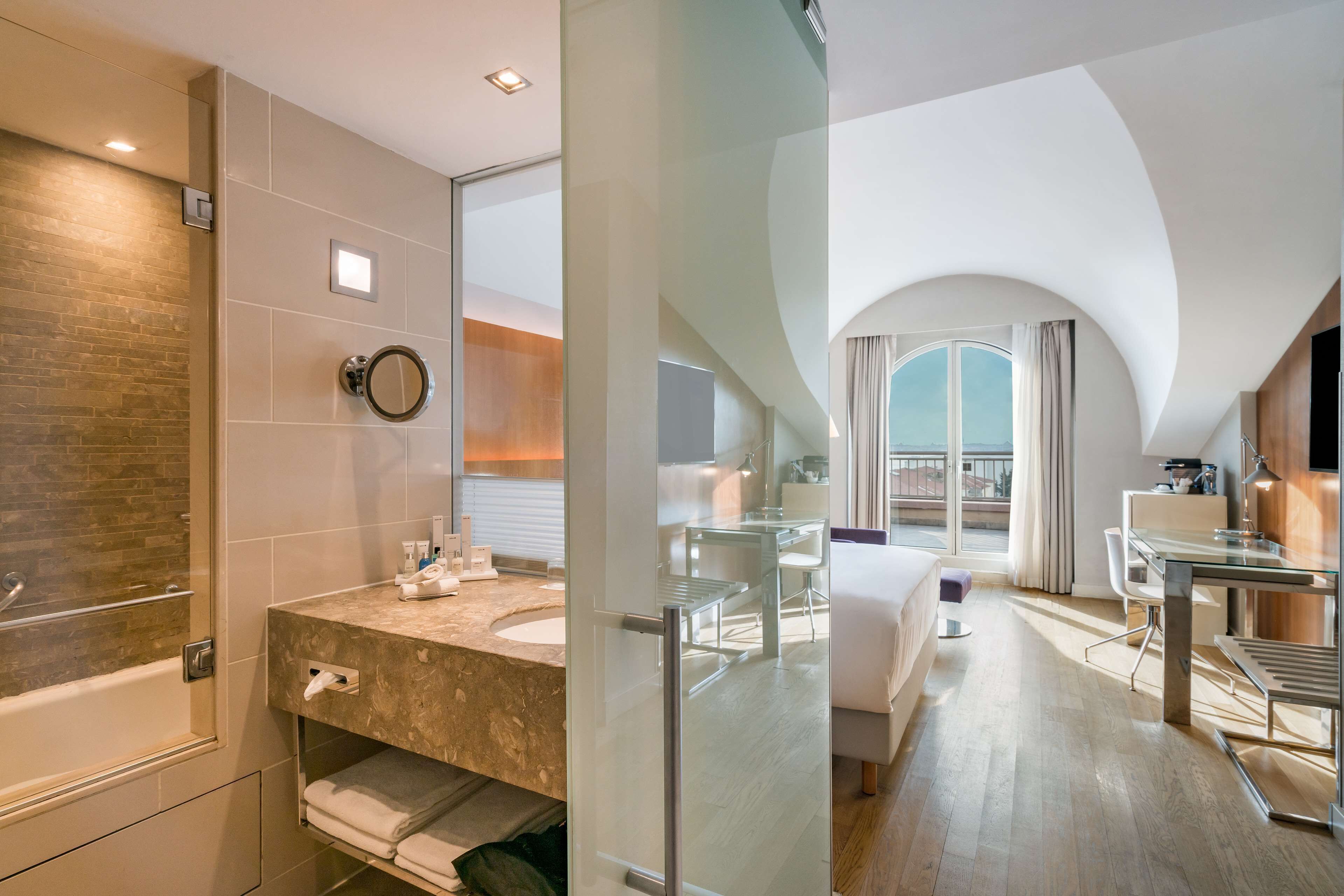 A modern hotel bathroom with a bathtub, a glass-enclosed shower, and a vanity with a mirror.