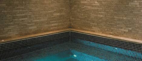 A small, rectangular indoor pool with a tiled floor and walls, surrounded by a brick wall.
