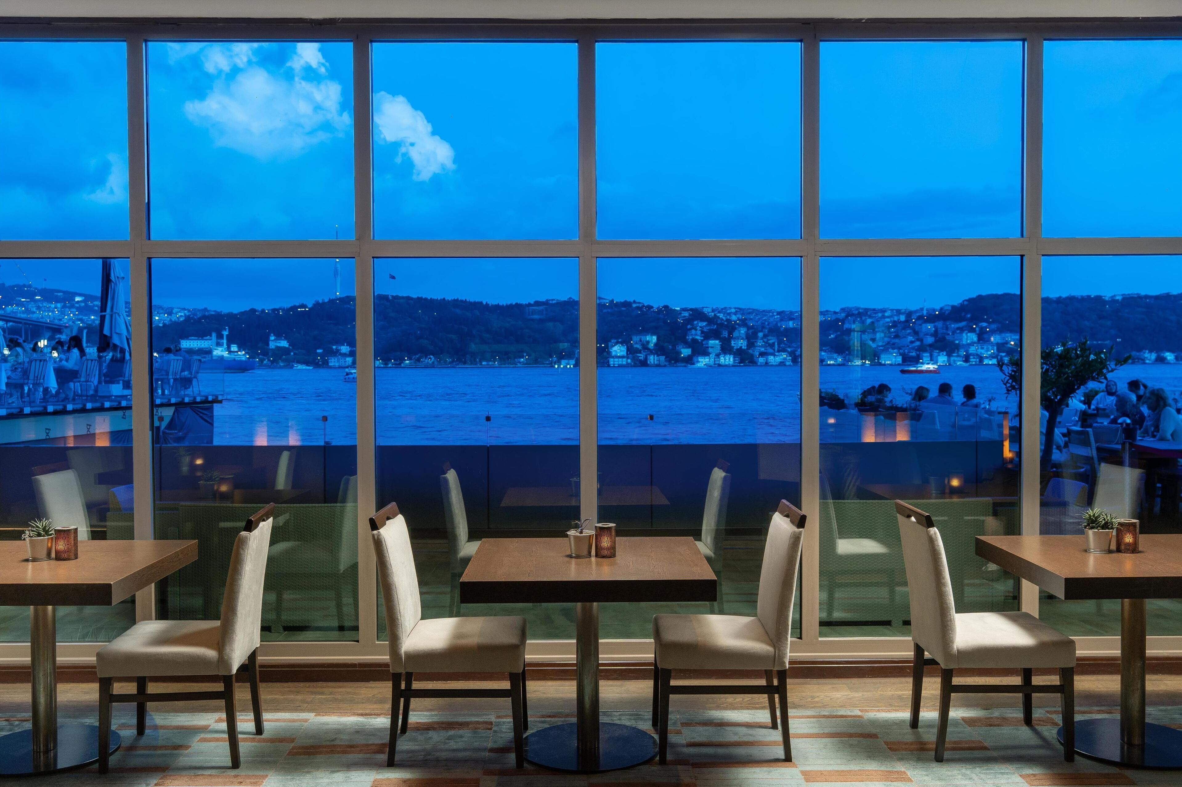 Un restaurant doté de grandes fenêtres donnant sur un paysage urbain avec vue sur le front de mer.