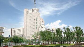 Un hotel alto con una torre destacada, rodeado de un área ajardinada con árboles y un césped bien cuidado.