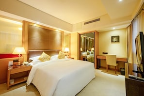 A hotel room with a large bed, bedside tables with lamps, a desk, a chair, a television, and a mirror.
