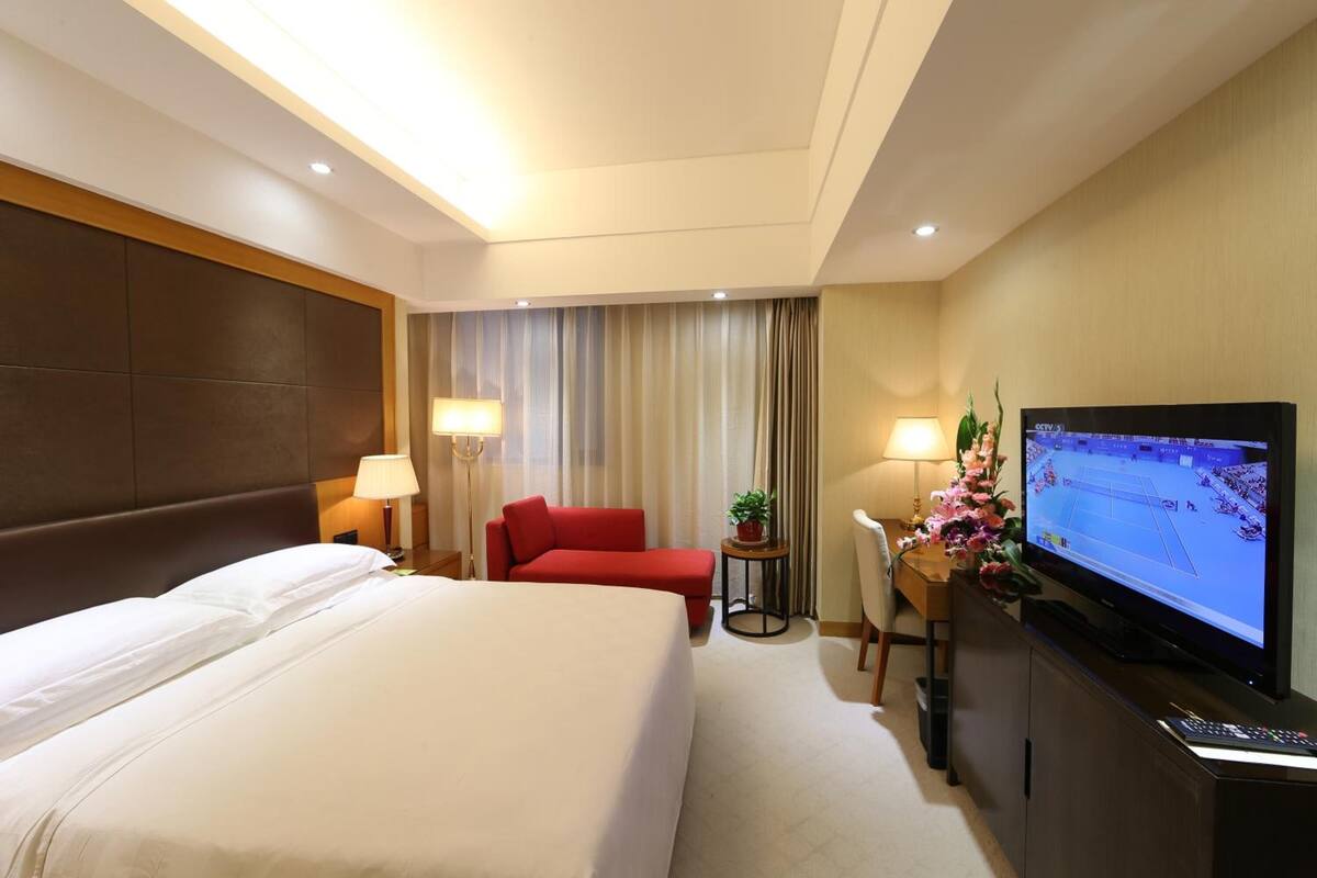 A hotel room with a large bed, a red sofa, a desk with a TV, and a curtain.