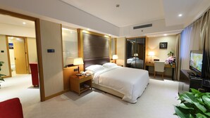 A hotel room with a large bed, bedside tables with lamps, a desk with a chair, a TV, and a mirror.