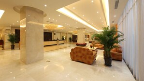A spacious lobby with a marble floor, a reception desk, a sofa, and potted plants.