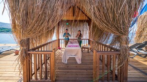 Une terrasse en bois surmontée d’une structure à toit de chaume, avec une table de massage et des chaises longues.
