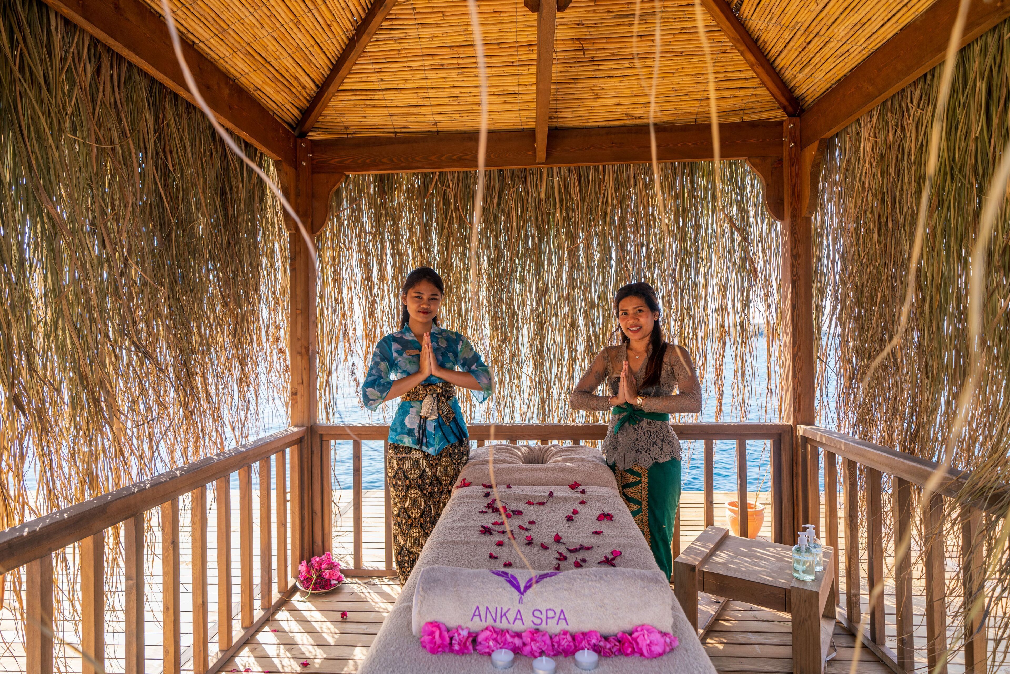 A wooden deck with a massage table labeled "Anka Spa," surrounded by bamboo walls and a railing.