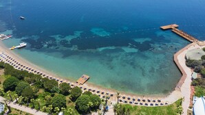 Vue aérienne d’une zone côtière avec une eau d’un bleu limpide, une jetée et une plage bordée de rangées de parasols.