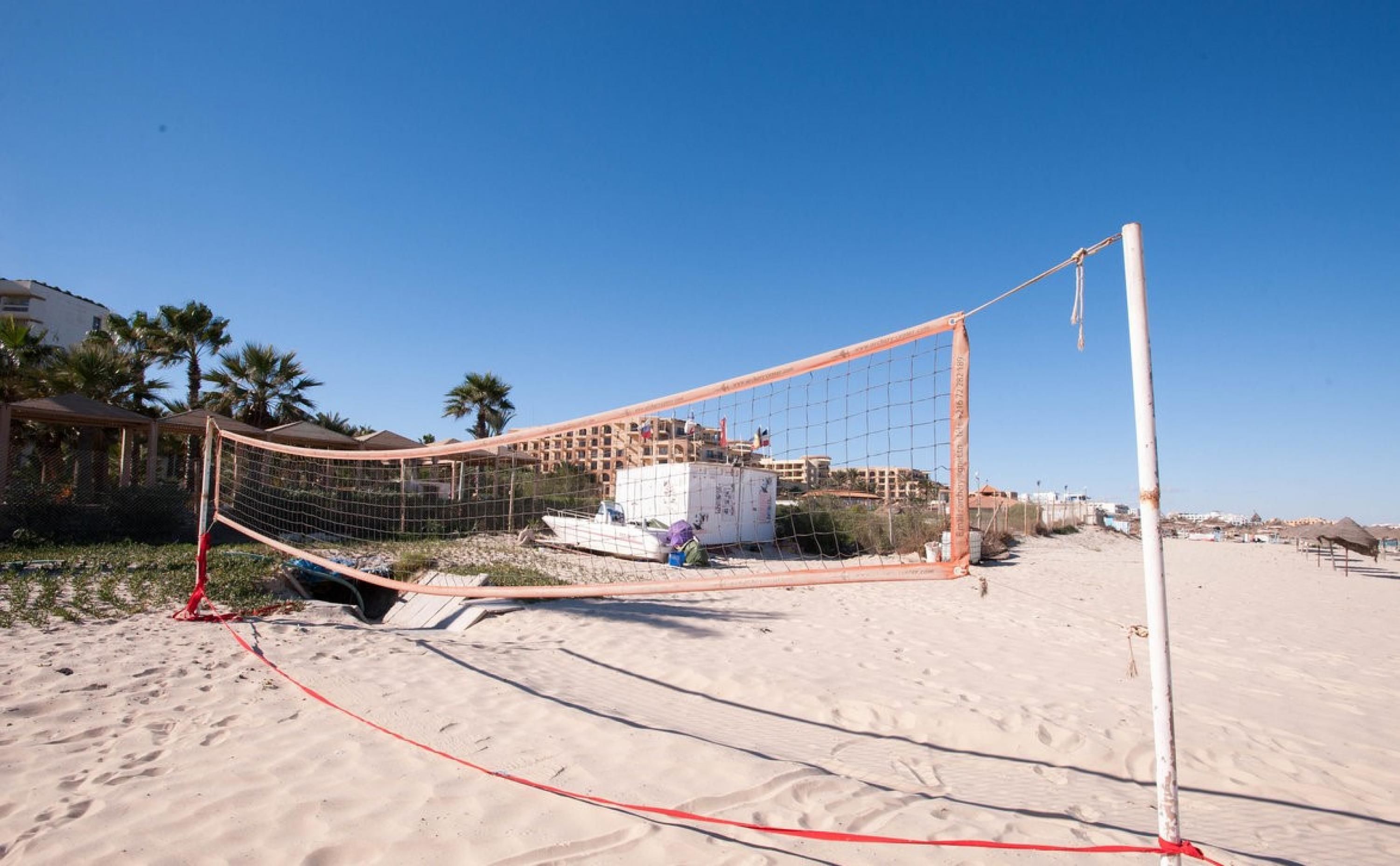 A beach volleyball net set up on a sandy beach with a building in the background.