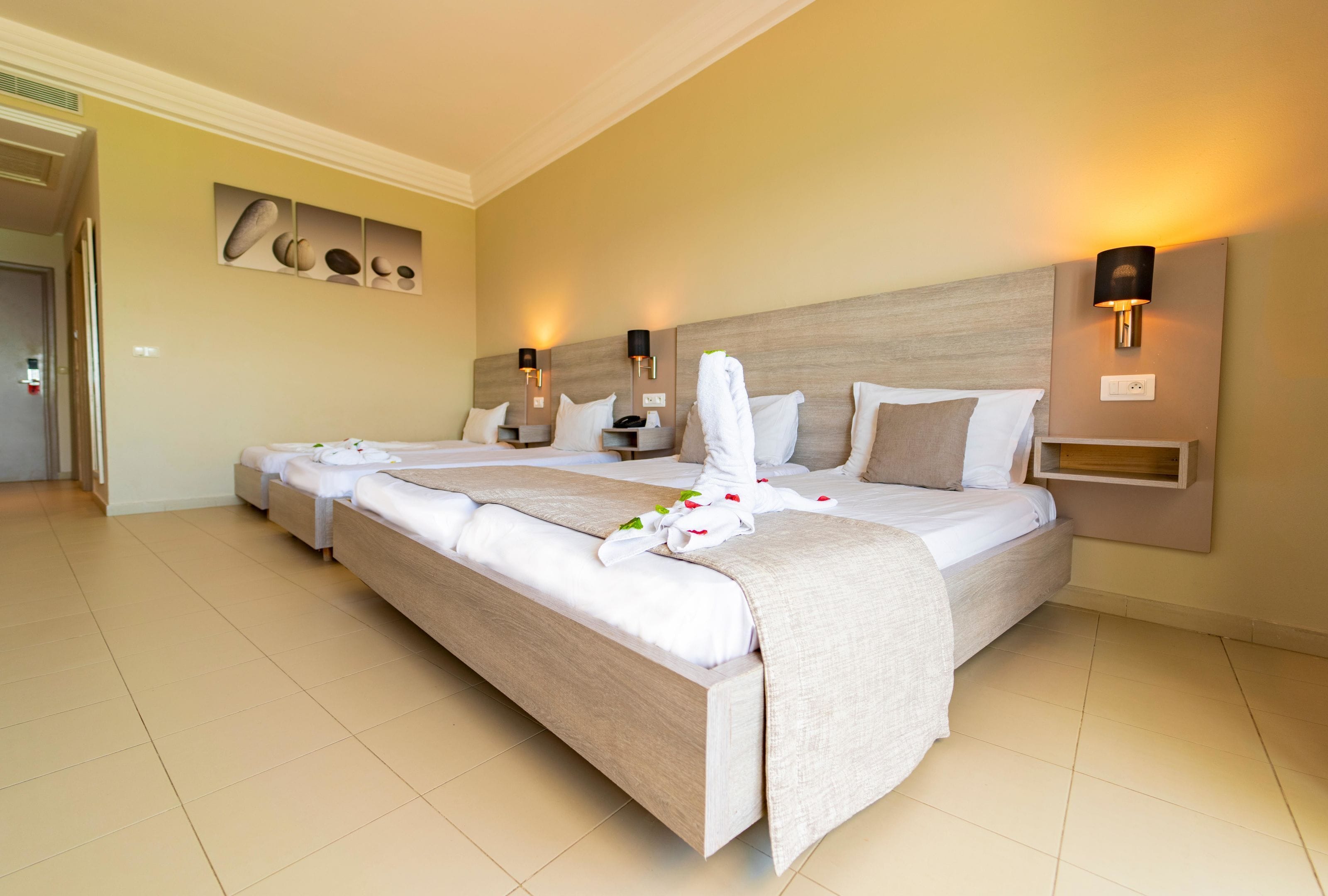 A hotel room with a large bed, two bedside tables, wall-mounted lamps, and a painting on the wall.