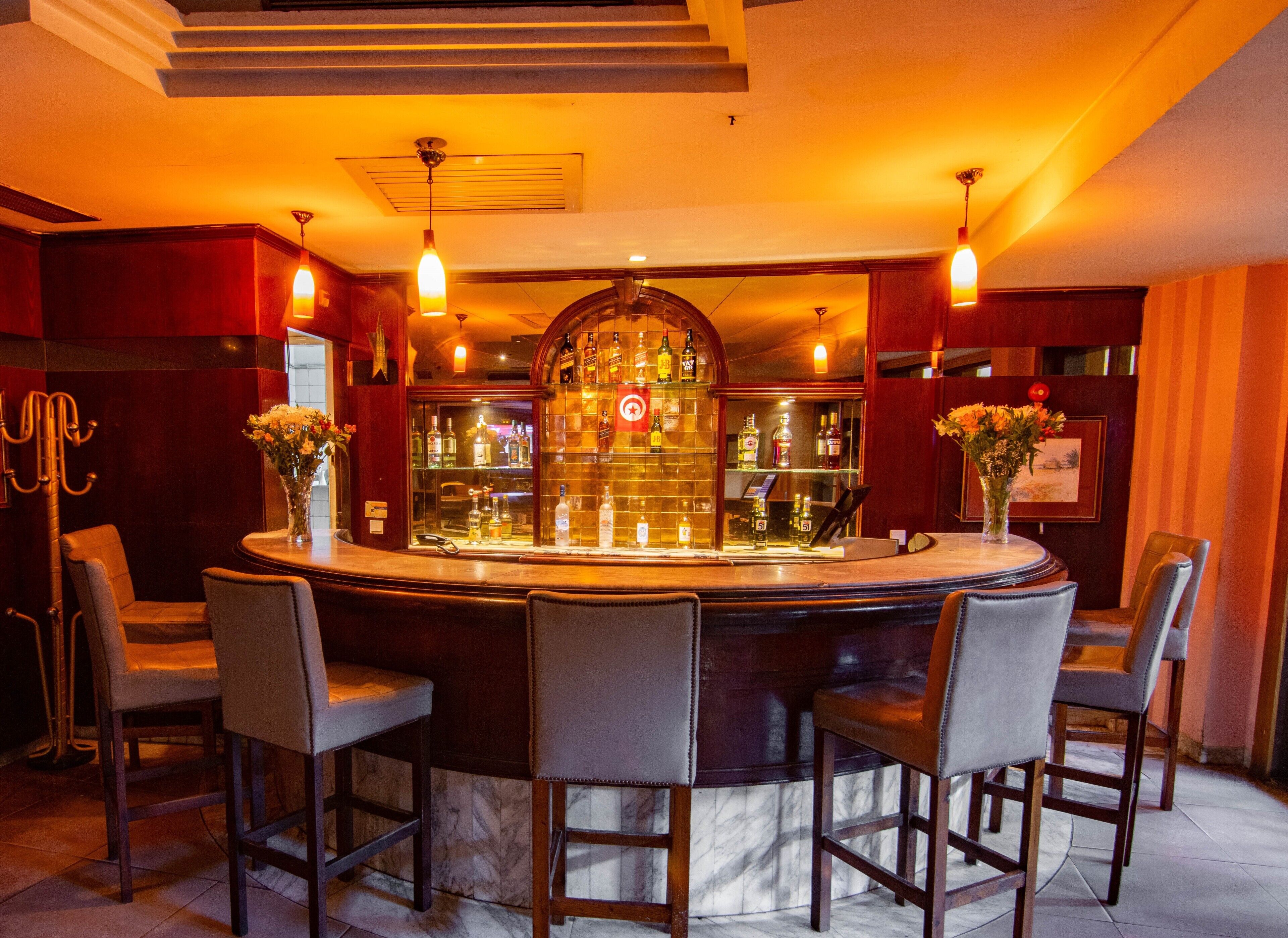 A bar area with a round bar, multiple chairs, and a display of liquor bottles.