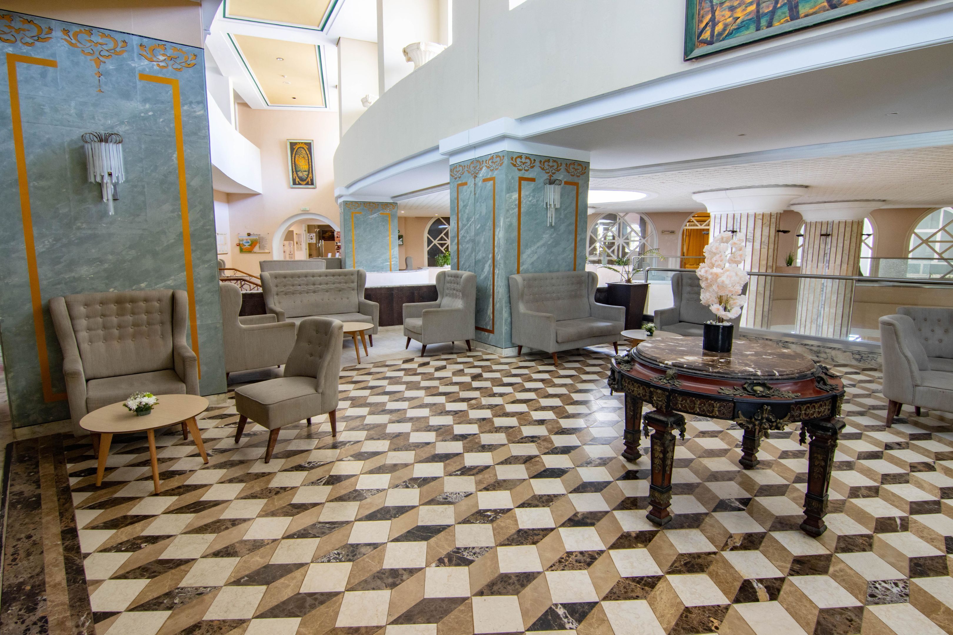 Um hall amplo com piso xadrez, assentos confortáveis e uma mesa decorativa.