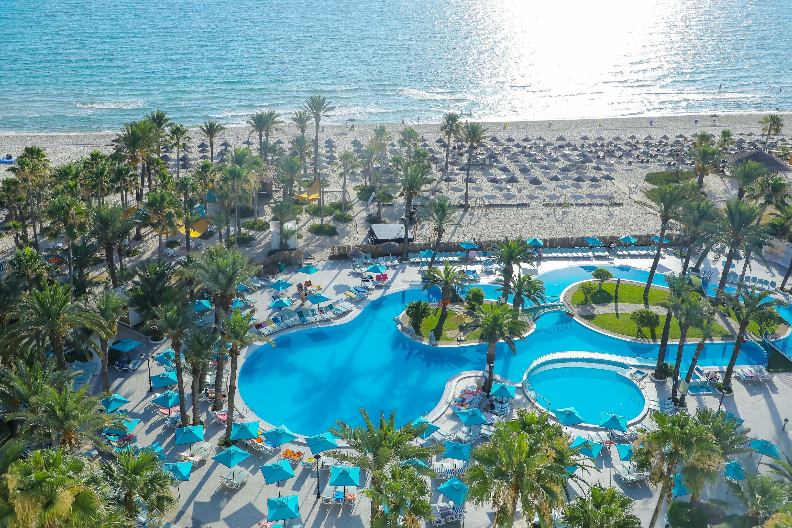 A resort with a large pool area, beach access, and palm trees.