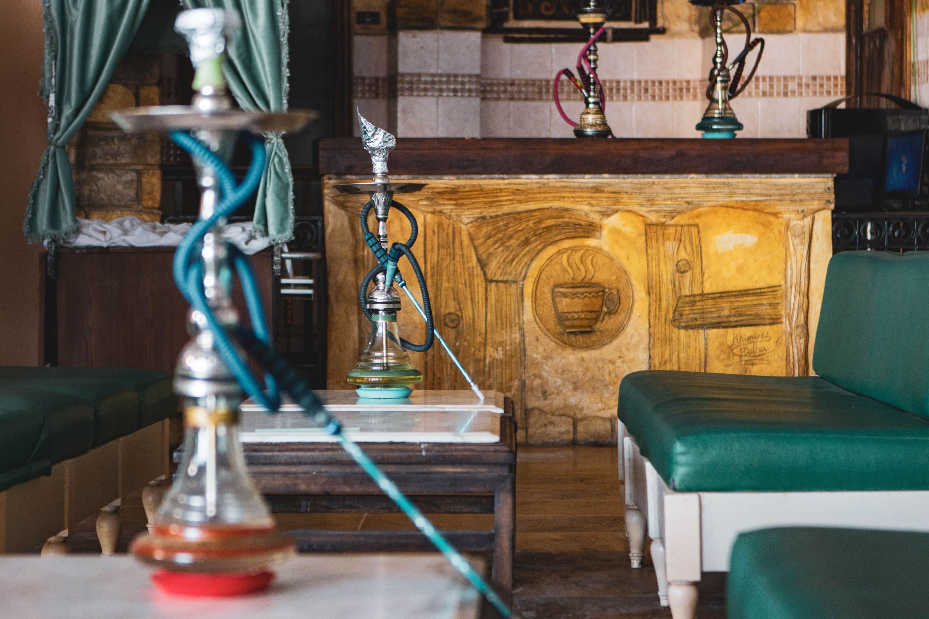 A room with a wooden cabinet, a green cushioned bench, and a hookah on a table.