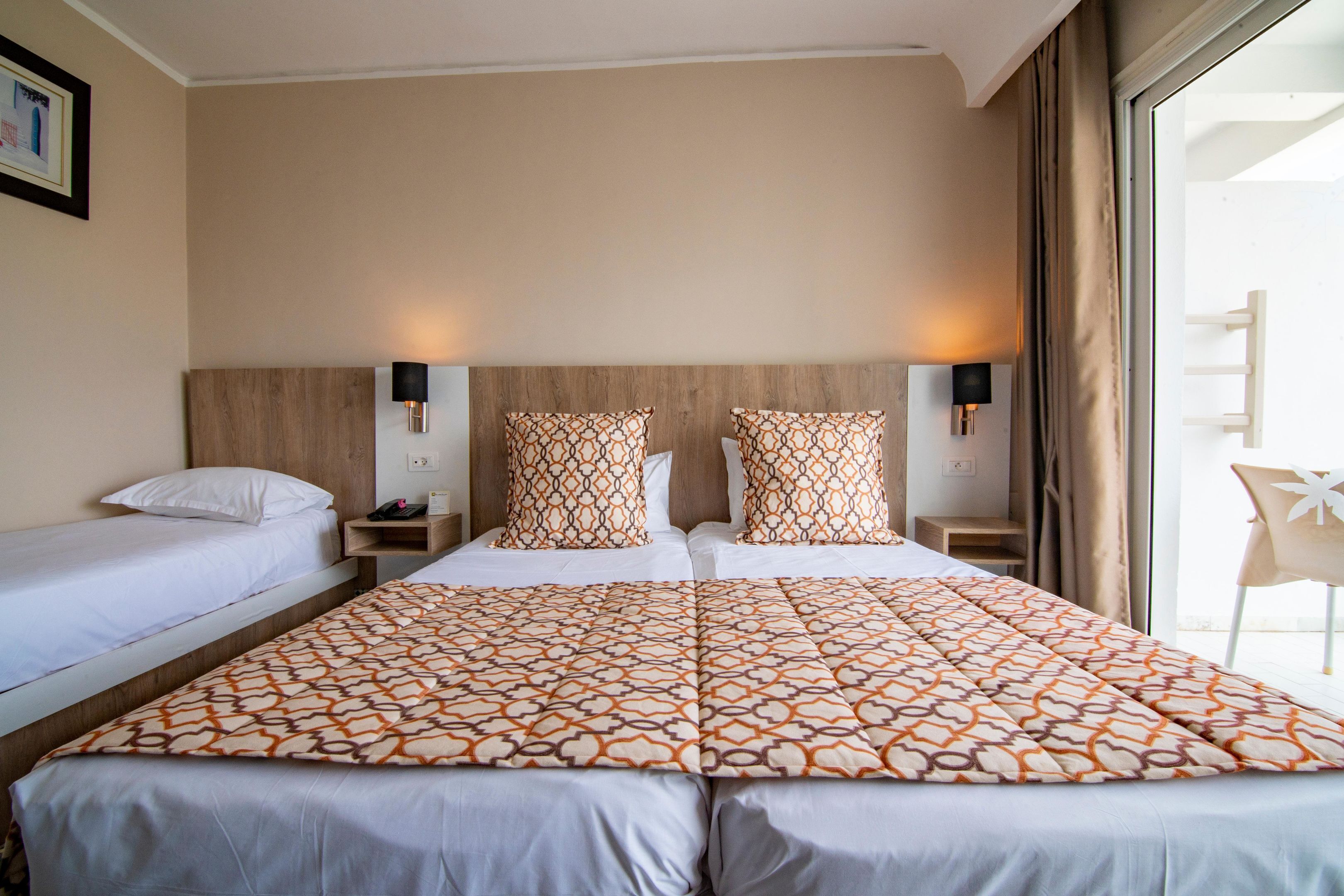 A hotel room with two beds, a large bed with patterned bedding and two smaller beds with plain bedding.