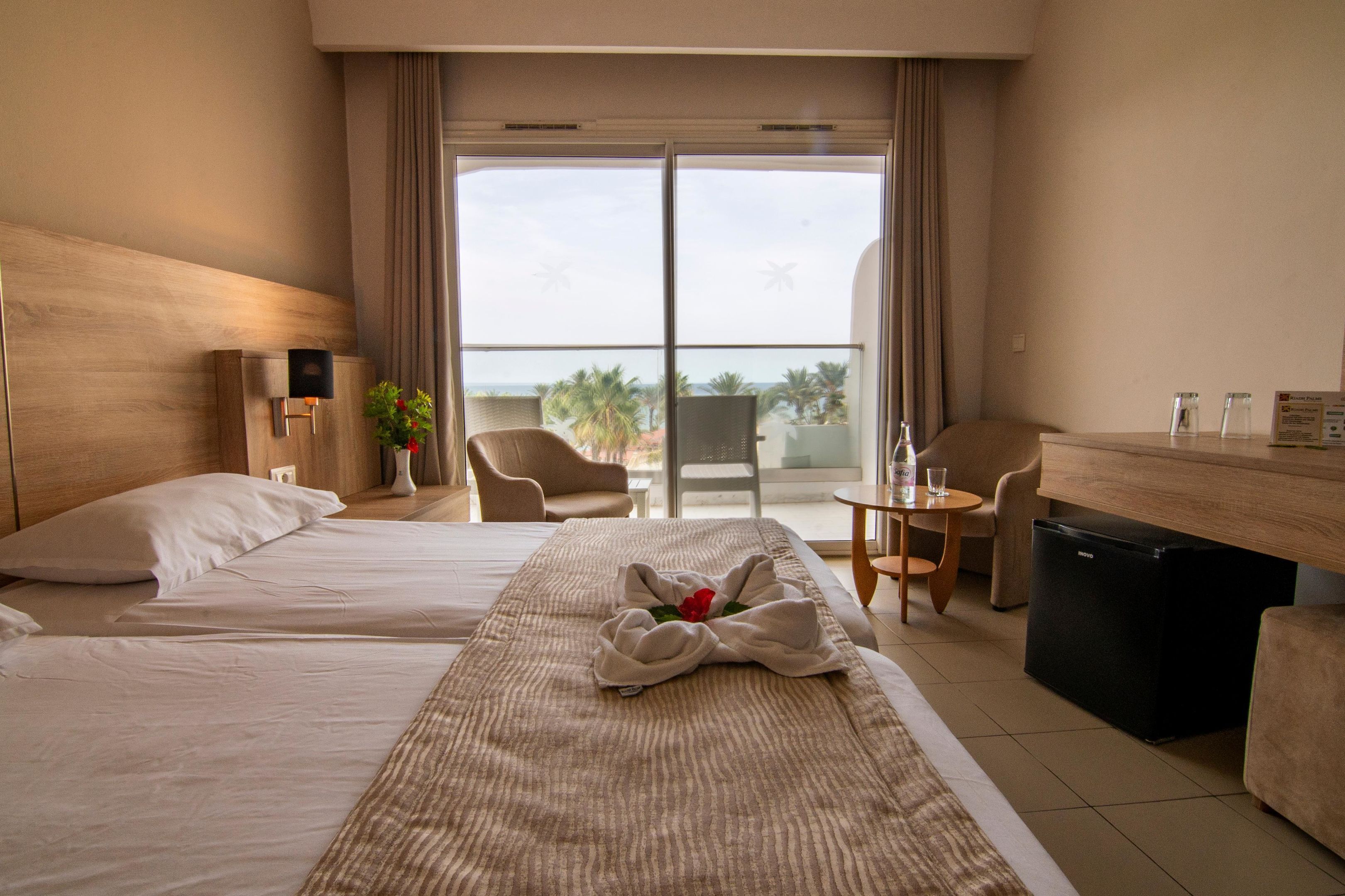 Una camera d'albergo con due letti, una scrivania, una sedia, un tavolino e vista sull'oceano.