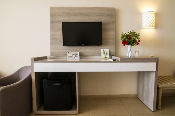 A hotel reception desk with a flat-screen TV, a flower vase, a trash bin, and a wall-mounted light fixture.